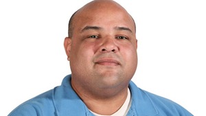 professor wearing a blue polo shirt in front of a white backdrop